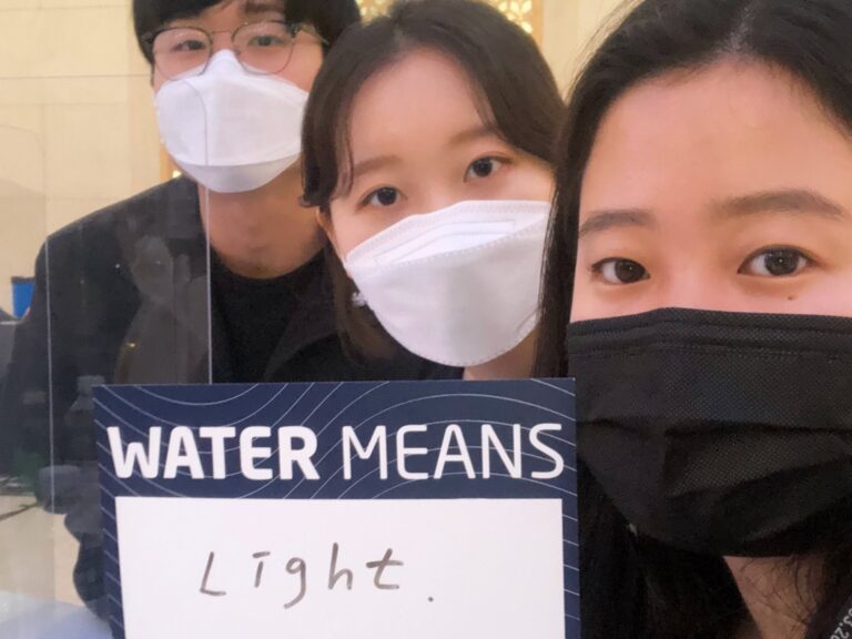 Three Korean participants with a sign stating "Water Means - Life"